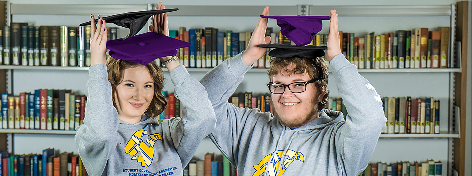two students holding two graduation caps each