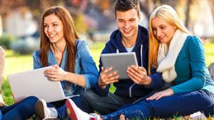 Three student on lawn looking at laptop