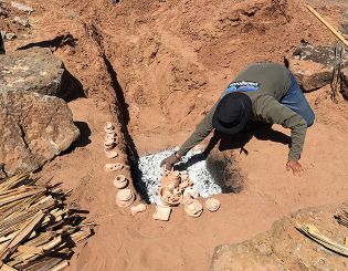 Adrian places pottery in the fire pit.